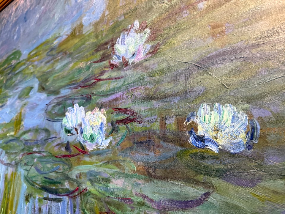 Closeup of painted water lilies that shows the broad textured brush strokes and unexpected colors (purples and maroons) that when viewed from a distance creates the illusion of greenery.