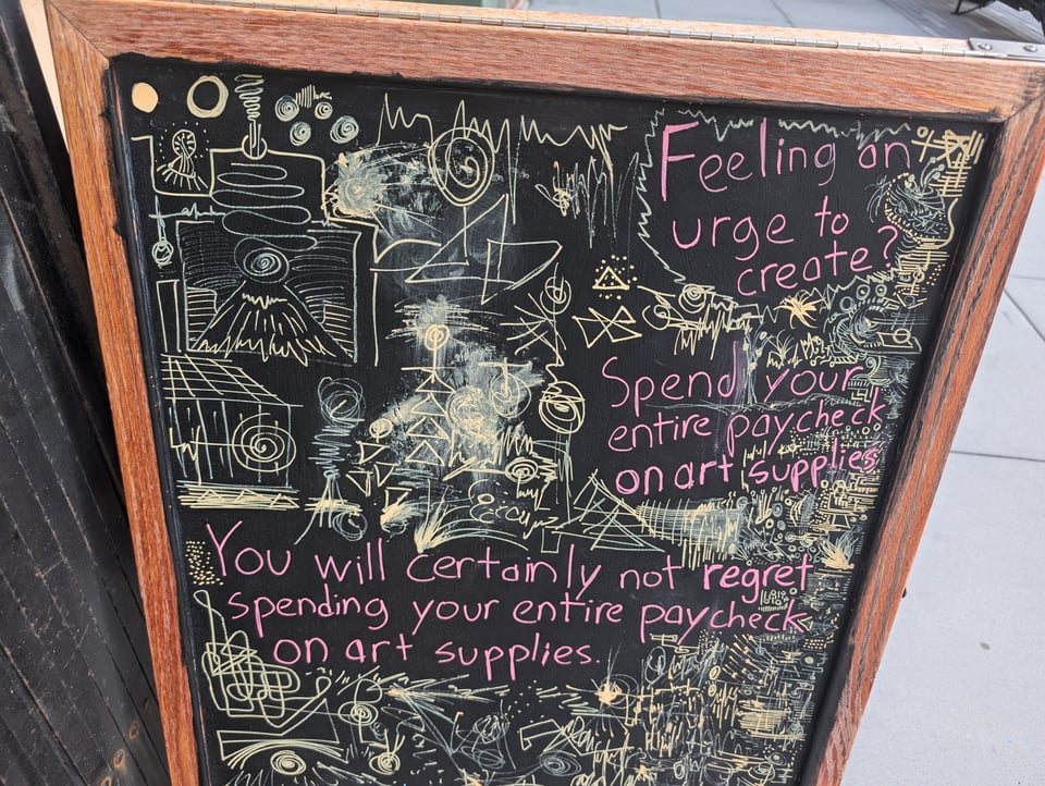 A chalkboard with a bunch of weird squiggles and designs, plus the words Feeling an urge to create? spend your entire paycheck on art supplies. You certainly will not regret spending your entire paycheck on art supplies