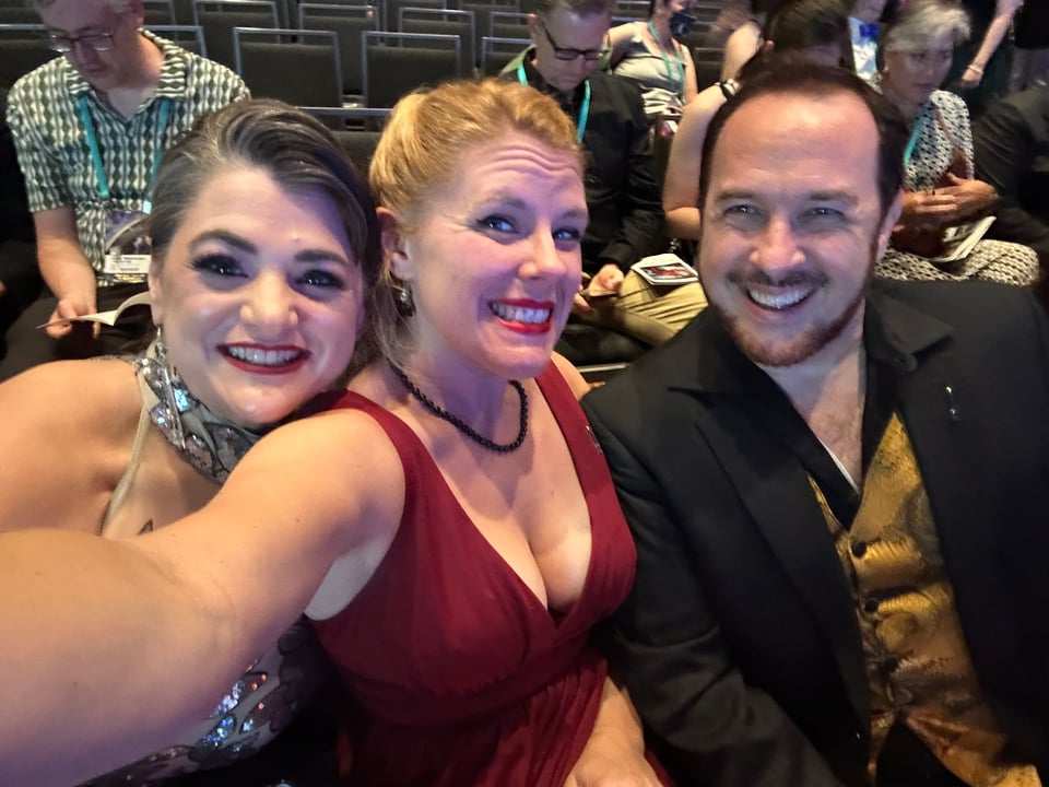 Cass sitting in the auditorium for the Hugo Award Ceremony, flanked by her co-hosts, Natania Barron and Marshall Ryan Maresca. They all look extremely spiffy.