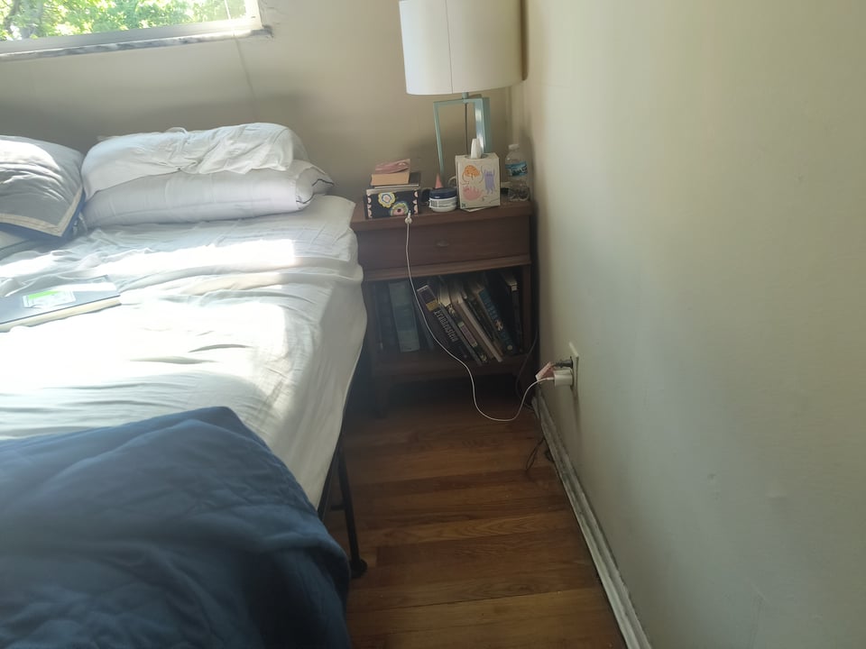 Picture of a nightstand next to a bed with a shelf containing several more books that have yet to be packed up.