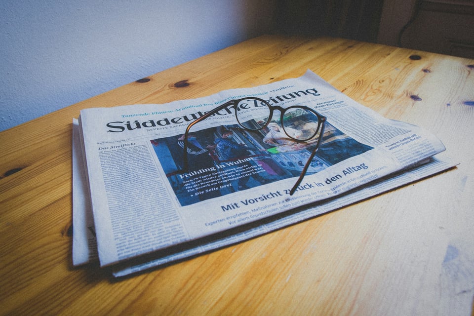 A man, seated, reads a newspaper. Photo by Ozan Safak on Unsplash.