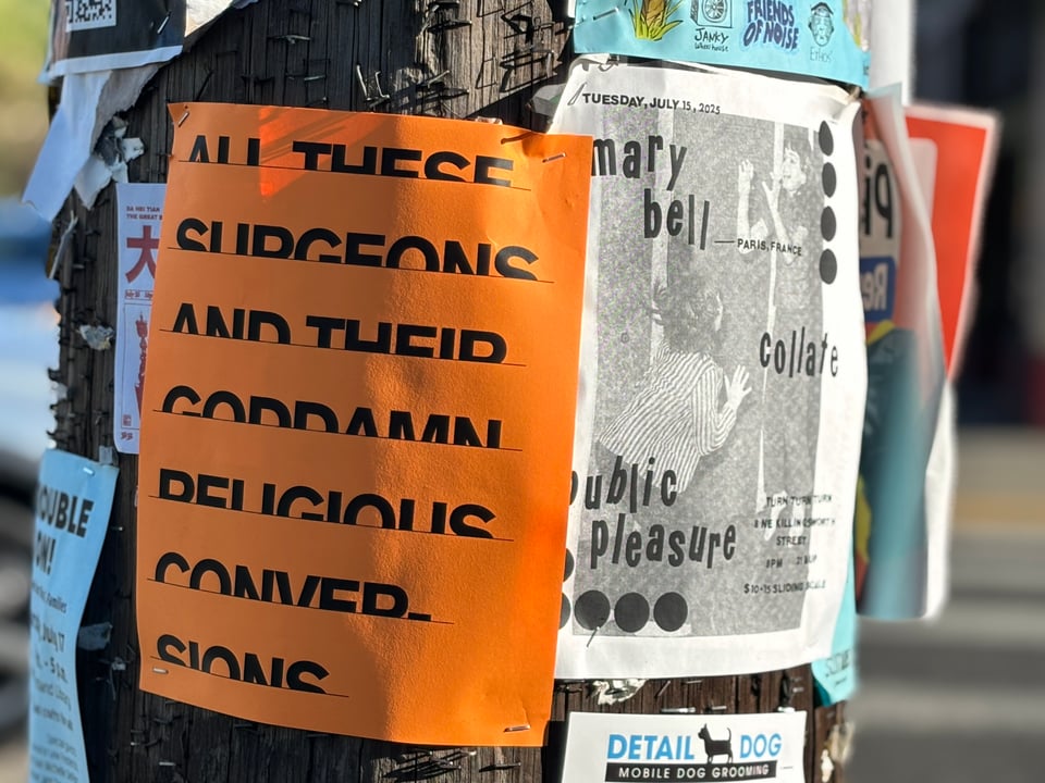 The text All these Surgeons and their Goddamn Religious Conversions in bold on a bright orange flyer stapled to a telephone pole