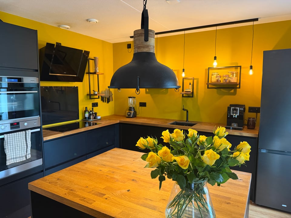 A sparse kitchen staged for real-estate viewings with a large bouquet of yellow roses on the kitchen island.