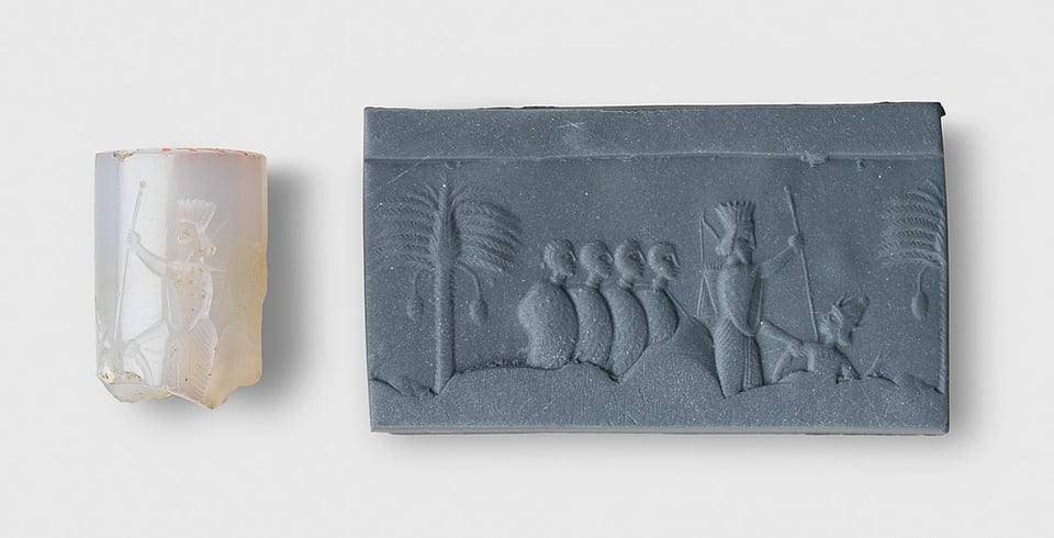 A light colored cylinder seal, broken at the bottom, beside a clay display revealing the image that has been engraved upon it. It shows a king killing a defeated enemy with a spear, while wearing a robe with flaring sleeves and a fluted crown. Behind the king is a row of bound prisoners who are also tied to each other by the neck. There is also a date palm with pendulous fruit in the background.