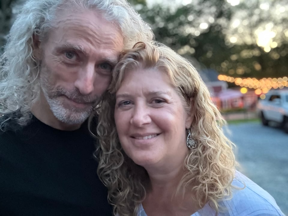 photo of white man and woman with long curly hair, standing in front of a restaurant's cinder parking lot