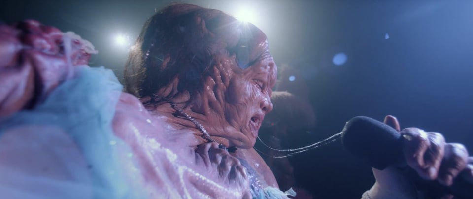 Monstro Elisasue speaks into a microphone.