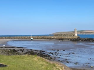 green grass in front of a rocky beach, water, a spit of land with a lighthouse at the end, and the ocean in the distance