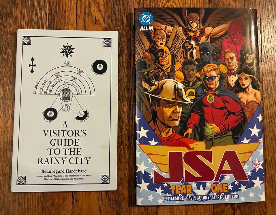 The books The Visitor's Guide to the Rainy City and JSA Year One, sitting on my floor.
