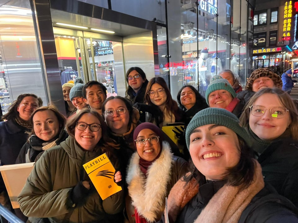 A group selfie, with people wrapped up warm in front of a New York shop, smiling at the camera and clutching Mincemeat yellow playbills.