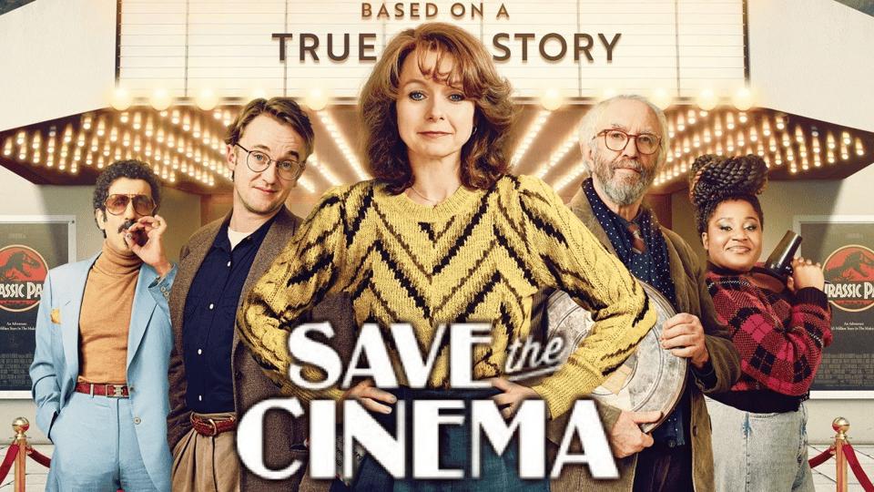 Photo: Film poster showing five people standing in front of a cinema with marquee lights. Centre: woman with auburn hair wearing a yellow jumper with black chevron pattern. Left to right: man in light blue suit with orange turtleneck and sunglasses, man in brown cardigan over navy shirt with glasses, the central woman, older bearded man in navy polka dot shirt holding what appears to be a rolled poster, Black woman with natural hair styled up wearing burgundy patterned outfit. Cinema entrance visible behind them with "Jurassic Park" posters on either side. White text overlaid reads "SAVE the CINEMA" with smaller text above reading "BASED ON A TRUE STORY". Red carpet barriers frame the bottom of the image.