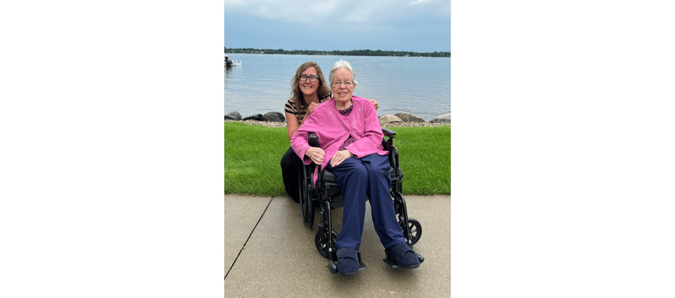 Katy behind Oma who is in a wheelchair in front of a lake