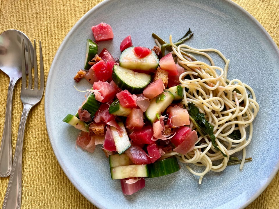 A blue plate with beet and cucumber salad and a small amount of spaghetti