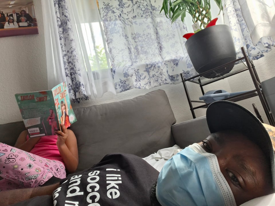 Nate wearing a mask babysitting his niece as she reads a book about Taylor Swift
