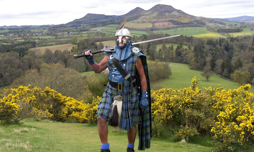 A man wearing tartan including a very fancy kilt, holding a huge sword and wearing a fierce helmet