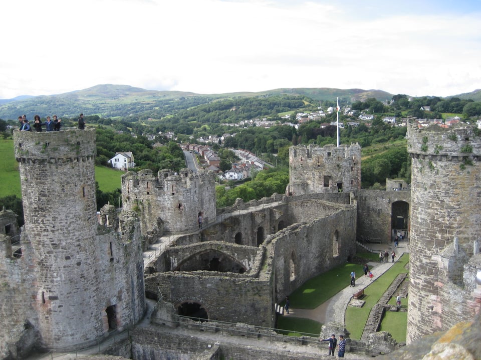 The interior of a stone castle, with intact walls but a missing roof, shot from the top of one of the castle's towers. Beyond are rolling hills.