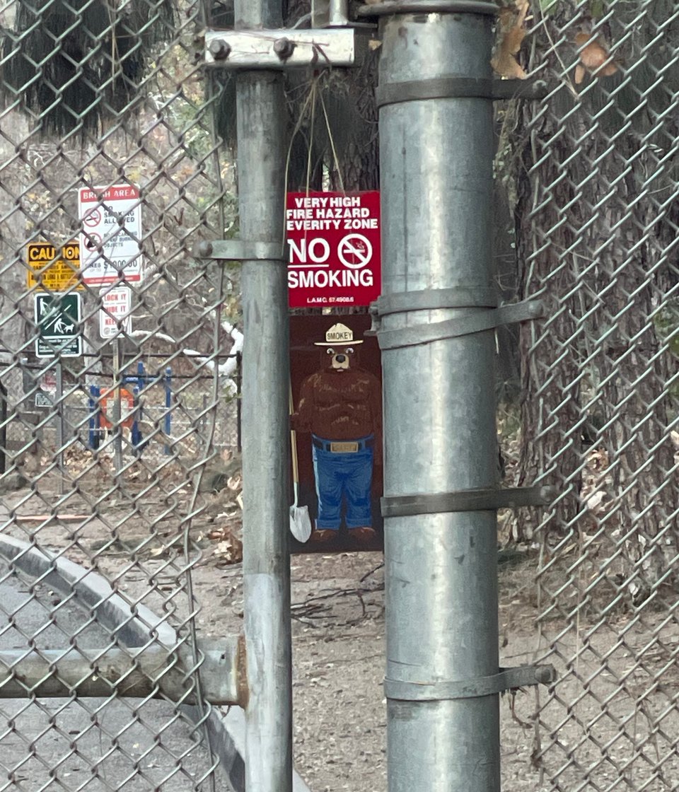 A picture of Smokey The Bear on a fire safety sign in Griffith Park seen through the closed fence gate