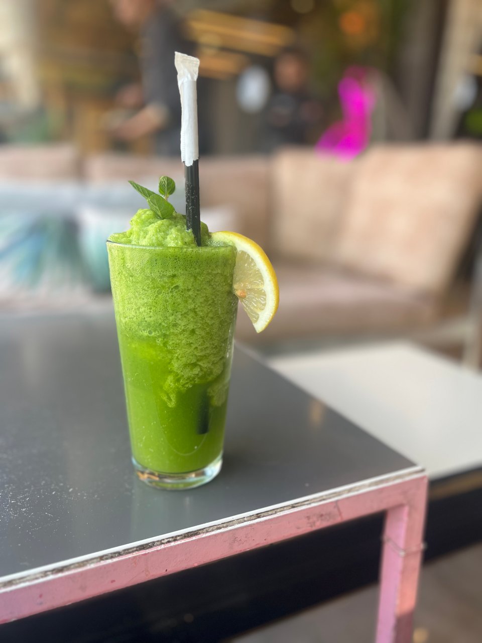 Bright green frozen drink in a tall glass, with a straw, a slice of lemon, and fresh mint