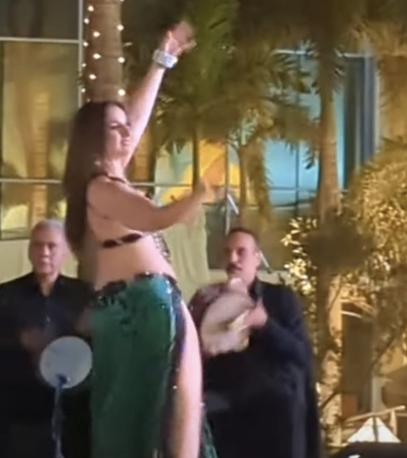 A dancer in green smiles to the side with two percussionists in the back
