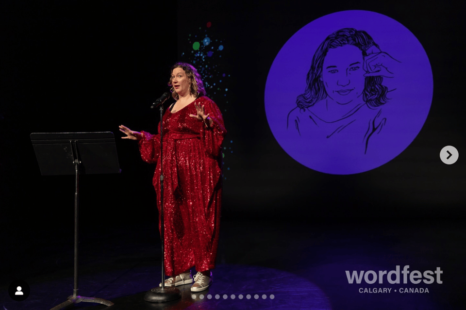 A white woman in a red sequinned jumpsuit stands on a stage, in front of a projected drawing of her own face