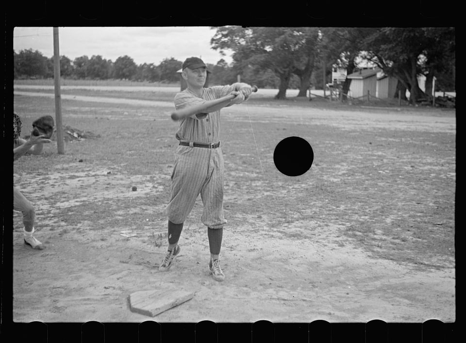 B&W image of a baseball player swinging on a dirt field