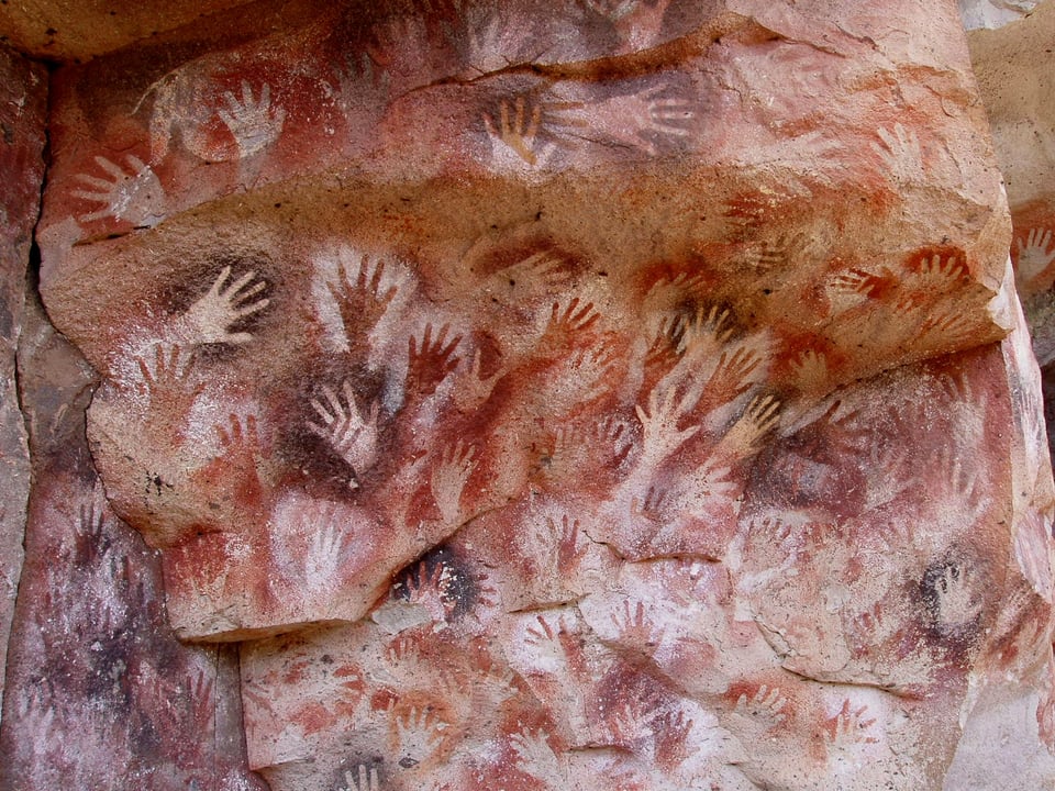 A image of the vibrant red, white, and brown handprints from Cueva de las Manos.