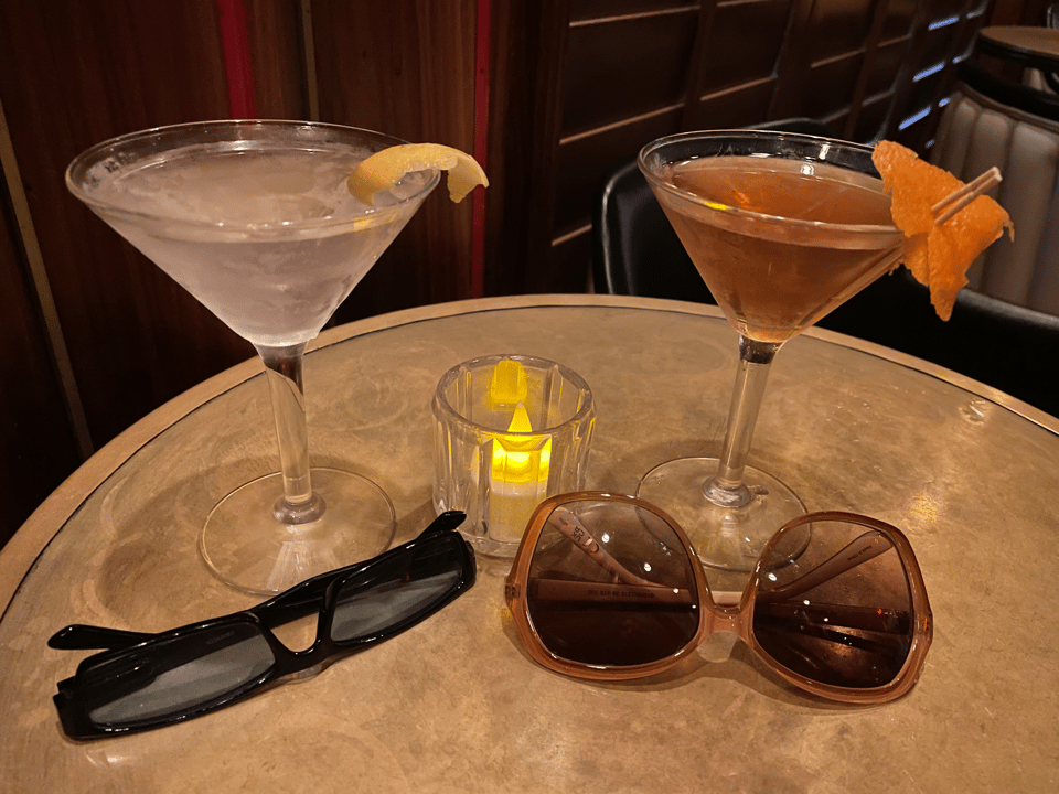 Two cocktails with matching pairs of sunglasses sit on a table at a bar