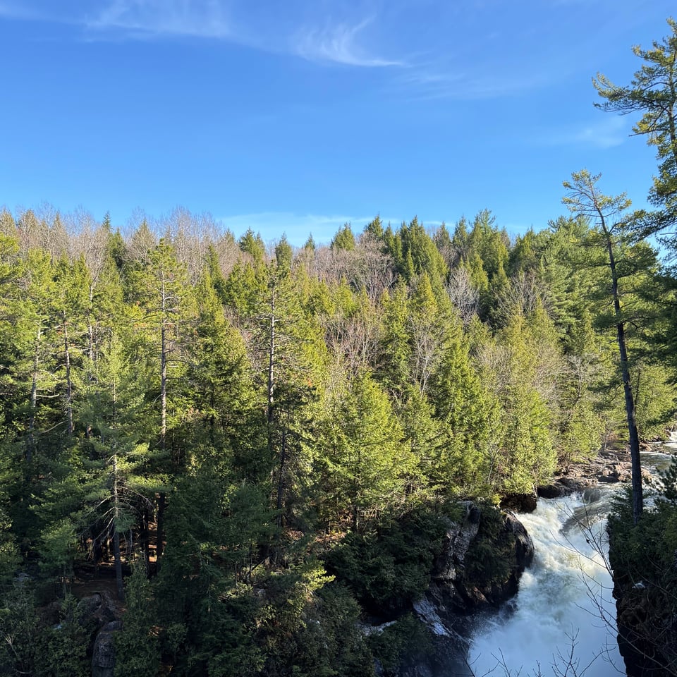 a cascading waterfall surrounded by green green trees under a blue sky in Quebec