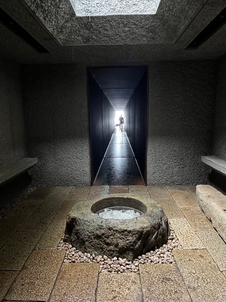 A stone bowl filled with shards of glass sits at the entrance to a long, dark tunnel with a person silhouetted in light at the end.