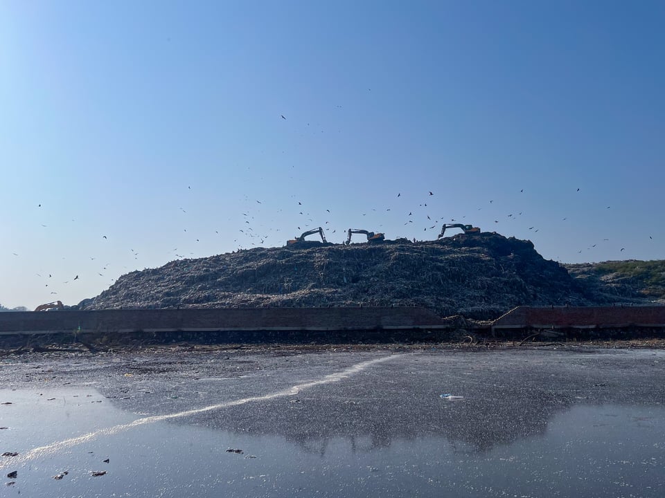 A garbage dump with three excavators on top, next to a lake