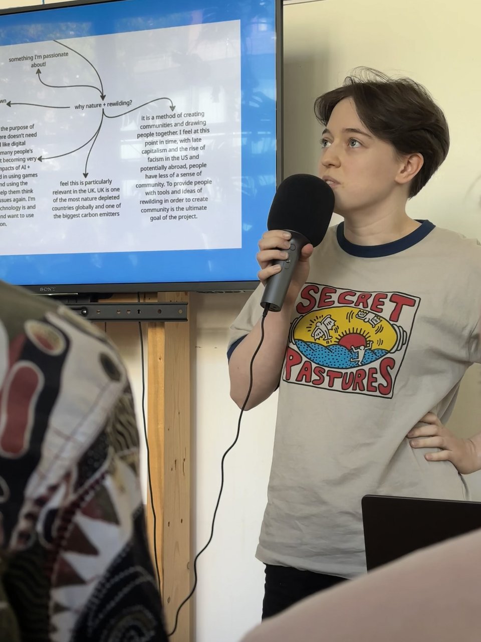 A thoughtful speaker. Slide behind her reads "why nature + rewilding"