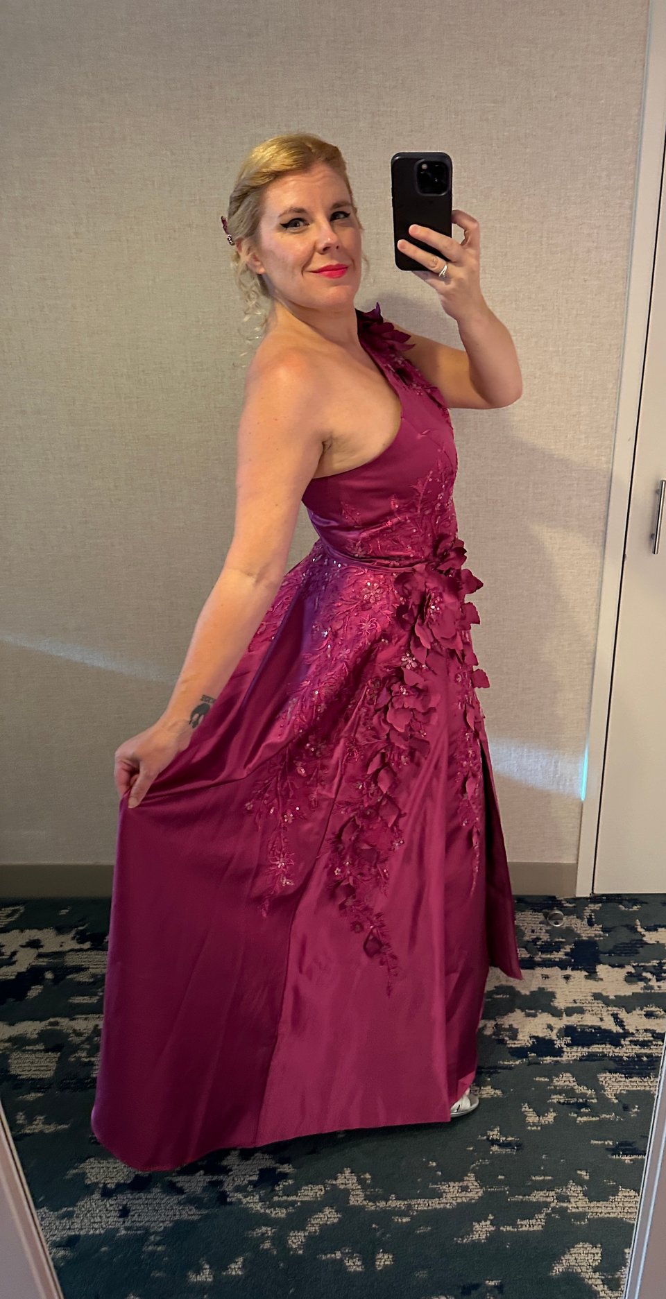 Mirror selfie of Cass in a fuchsia formal gown, one-shouldered, with floral appliques at the shoulder and spreading down the skirt from the waist. She's holding the skirt out to show it off. Her hair is rolled into a Gibson tuck with a few strategic curls bobbing about.