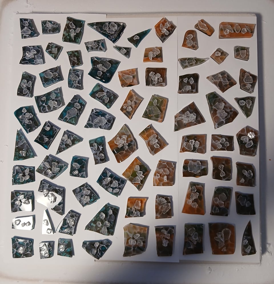 kiln shelf with a bunch of blue/brown glass pieces and a bunch of orange/green glass pieces with a bit of clear frit