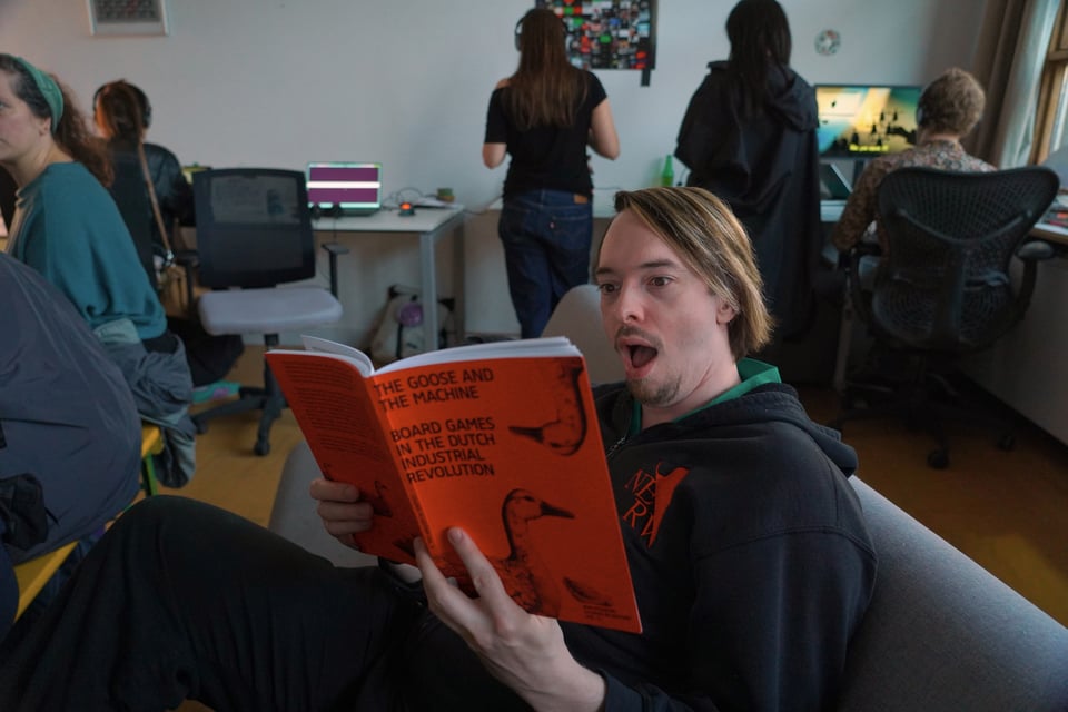 A man makes a shocked face as he reads a book titled "The Goose and the Machine"