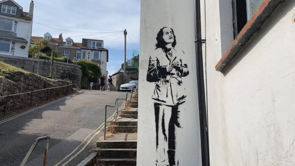 A stenciled graffiti of Barbara Hepworth on a narrow pale wall. She's in her signature trousers and jacket, hair scrapped back from her high forehead. She's looking up at something, smiling.