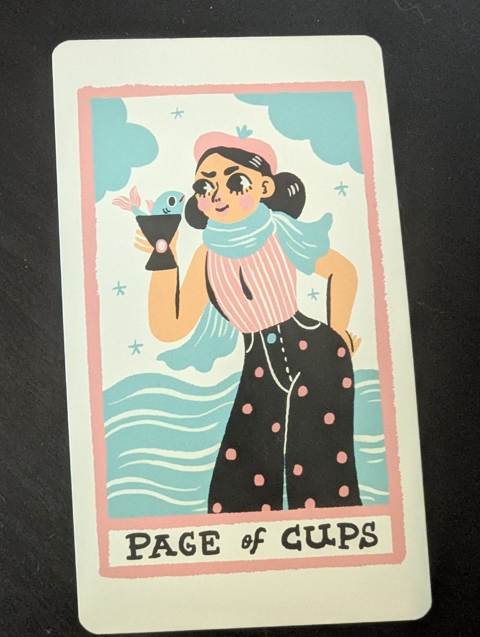 A feminine figure holding a fish in a cup. Text below reads: Page of Cups.