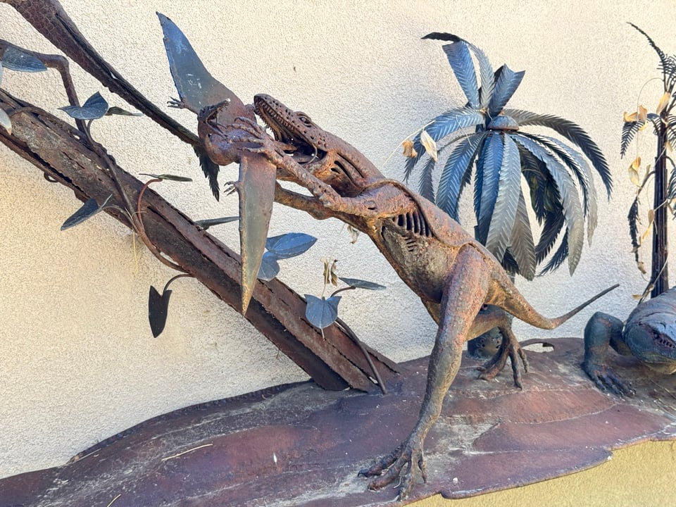 A metal sculpture showing a generalized theropod dinosaur reaching out to grab a small pterosaur, implying that catching prey like this led dinosaurs to evolve flapping arms.