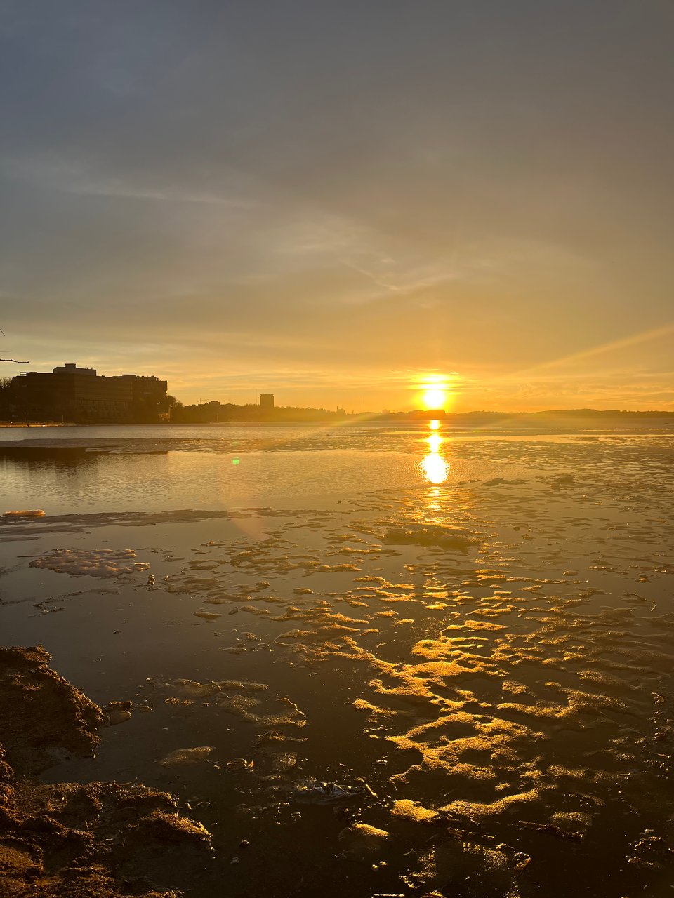gold sun sinking into the horizon and reflecting in the mostly melted lake scattered with ice