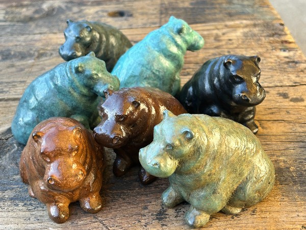 Seven small sculptures of sitting hippos in different patinas.