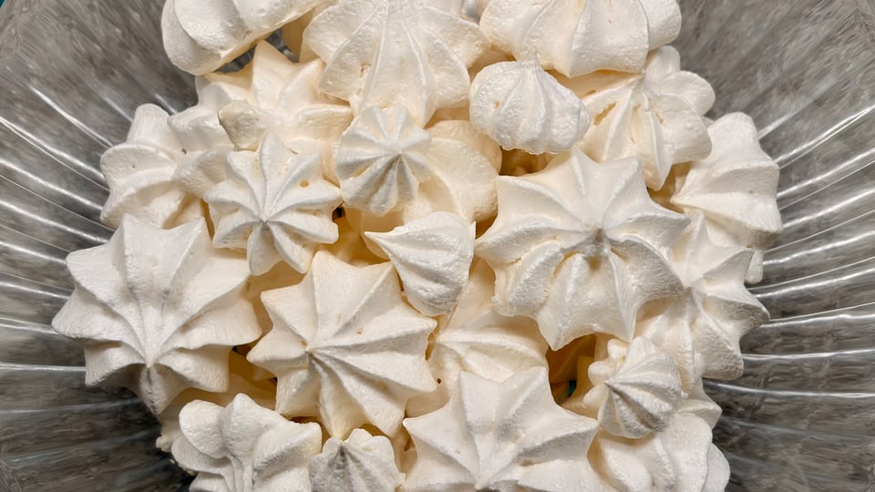 Close-up of a ribbed glass bowl with a mound of meringue kisses, piped as 8-point stars