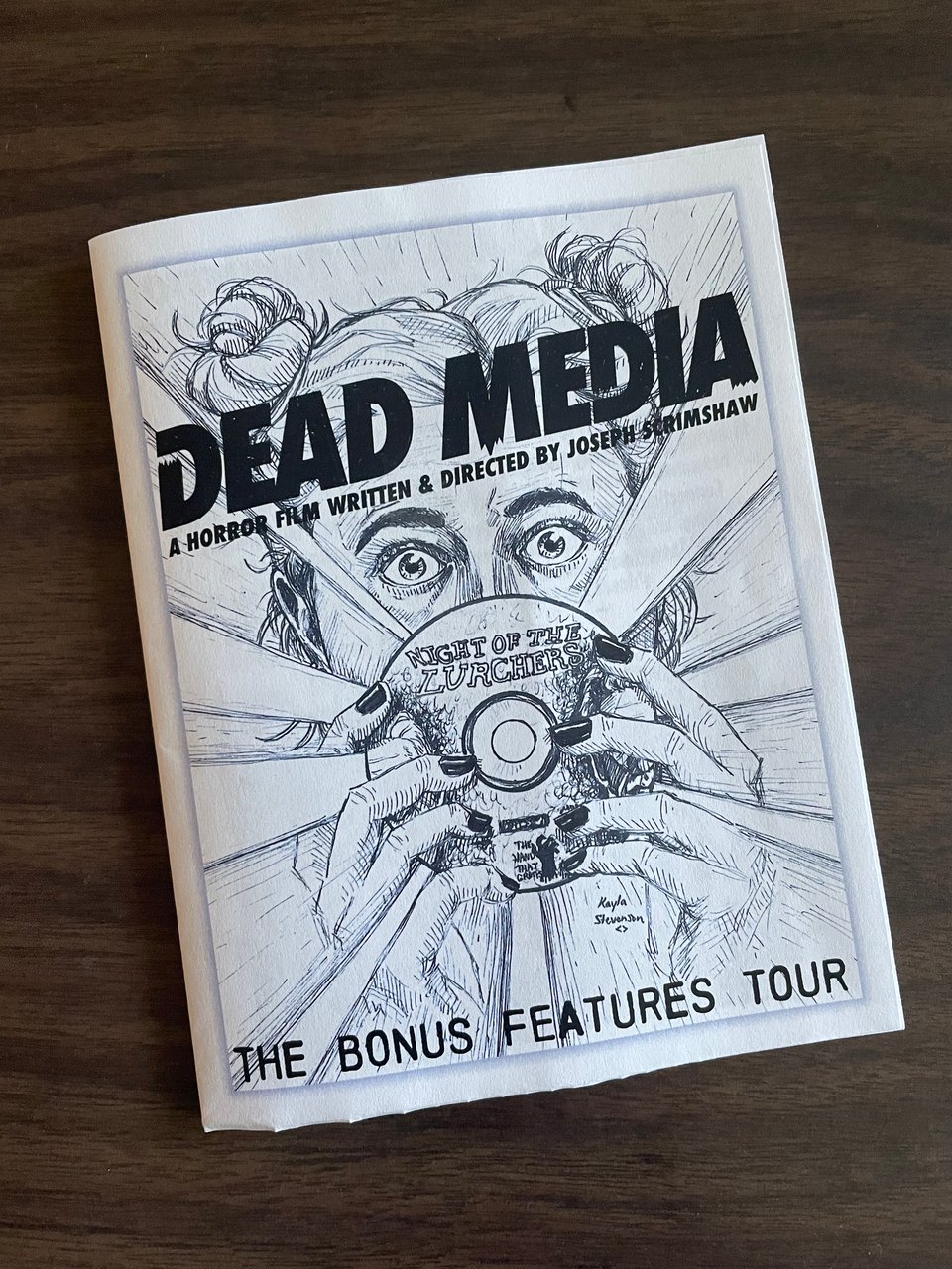 A small folded program. On the cover is the text Dead Media, a new horror film written and directed by Joseph Scrimshaw. The Bonus Features Tour. A pen and ink drawing of a stressed woman peering over a DVD with energy bursting out from the disc