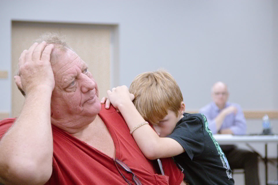 A boy leans on the shoulder of an older man, who has his palm on the side of his head.