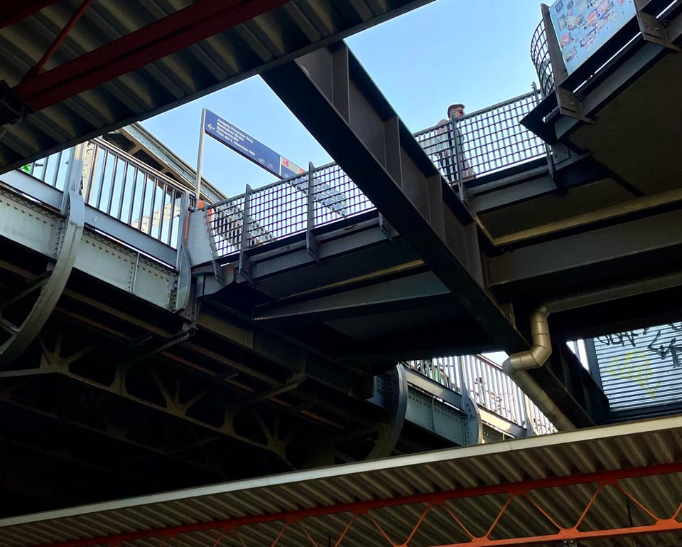 The picture tries to capture the multiple criss-crossing lines at one of the train stations looking up. There is a bridge, beams, shades, a foot bridge that connects to the entrance. A cornucopia of steel, if you will