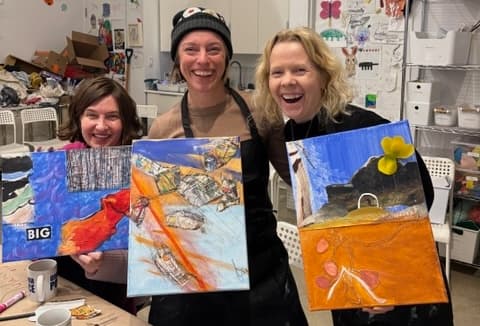 Three happy women holding up paintings in a studio
