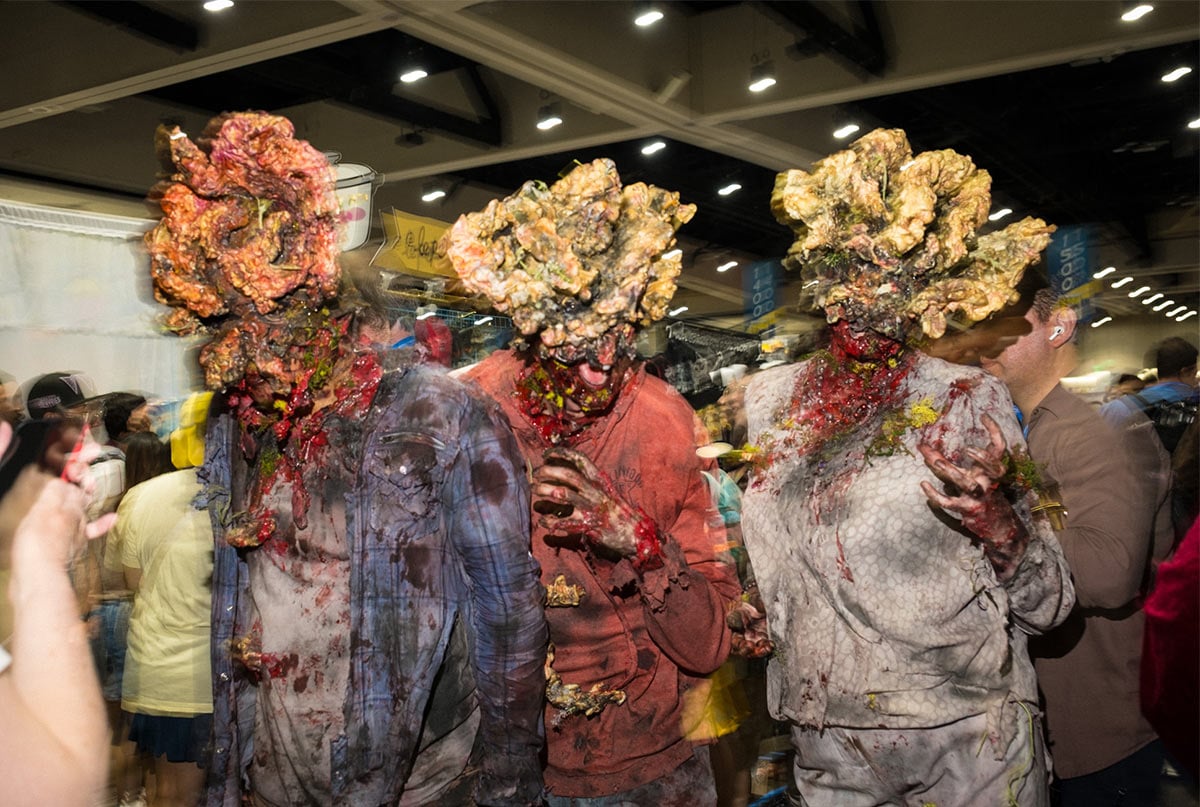 A group of three cosplayers dressed as the infected zombies from the Last of Us, their heads dressed in life-like prosthetics that make it appear as if fungus is splitting their heads open.