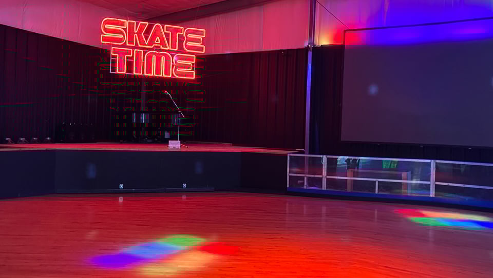 A neon sign reading "SKATE TIME" sits over a roller-skating rink lit up with colorful gel lights.