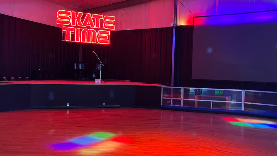 A neon sign reading "SKATE TIME" sits over a roller-skating rink lit up with colorful gel lights.