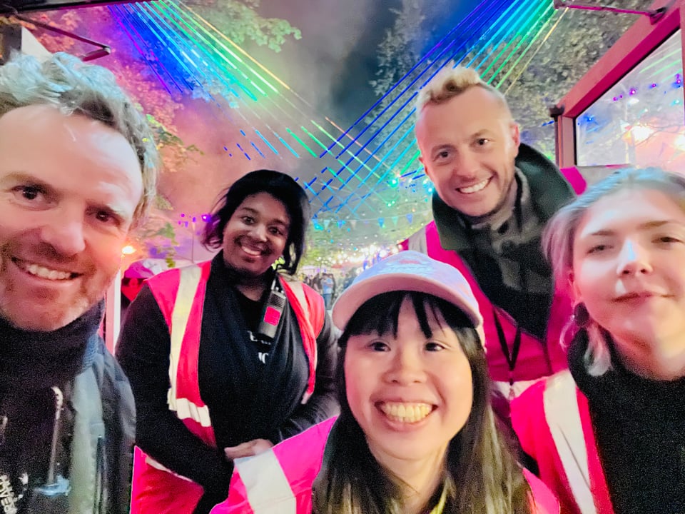 Five smiling crew members with rainbow lasers behind them