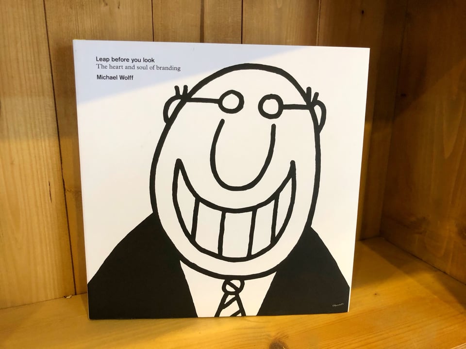Photograph of the book, "Look Before You Leap (The heart and soul of branding)" by Michael Wolff. The cover features a simple, black and white, cartoon illustration of a bald man wearing glasses and smiling a very toothy grin.