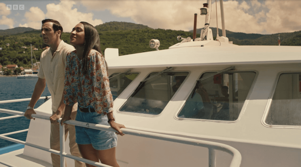 A white man and a black woman stand on the deck of a boat in a blue Caribbean sea.