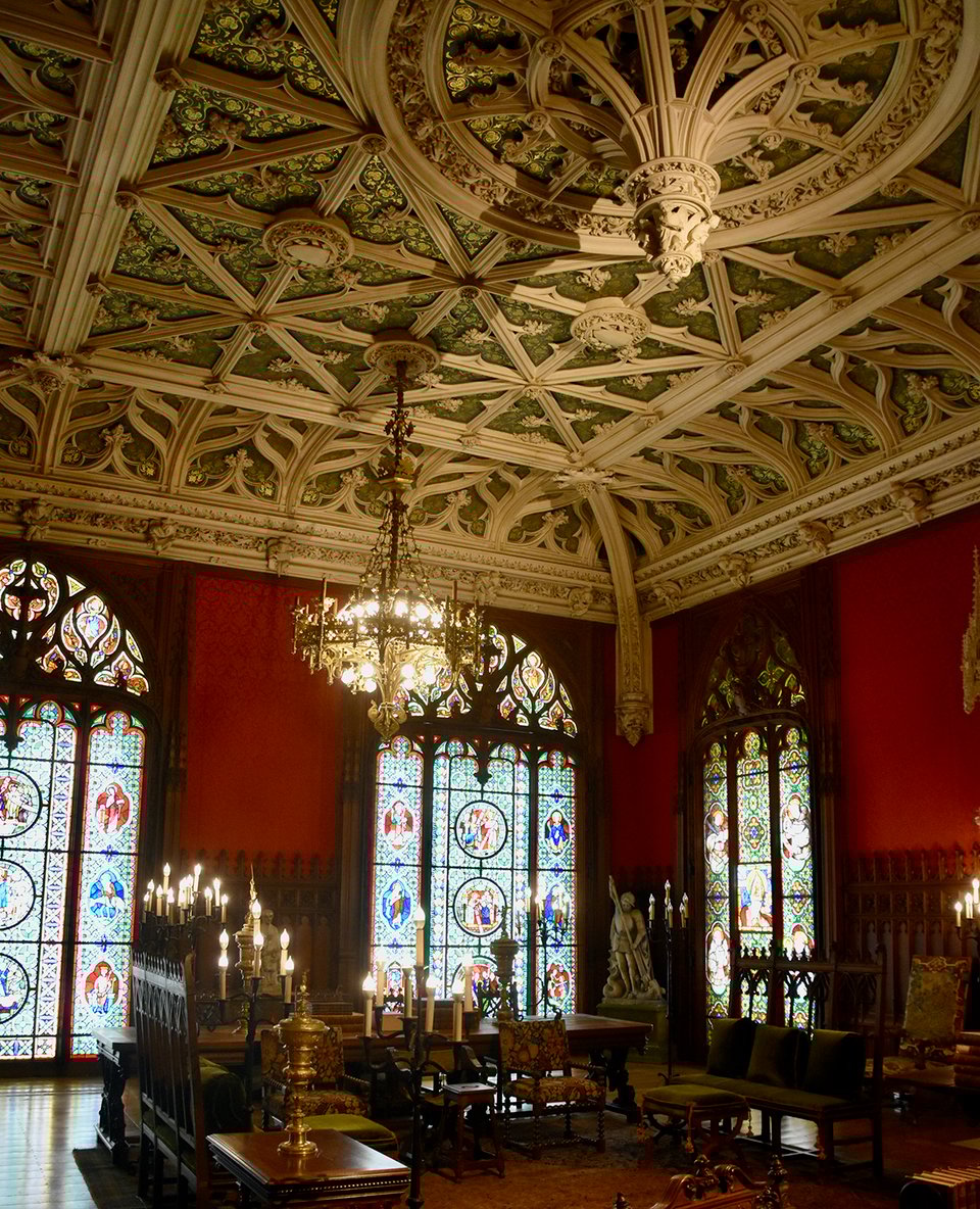 A dark library with stained glass windows and an ornate ceiling.